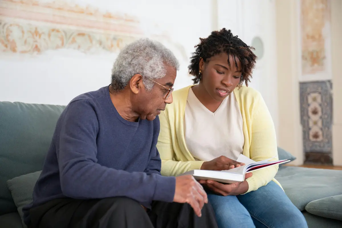 Registered Nurse and a patient reading a book on the couch, providing Senior & Elder Care in Belleville.