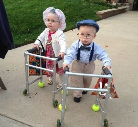 Young children dressed as seniors using PVC pipe walkers with tennis balls on the feet.